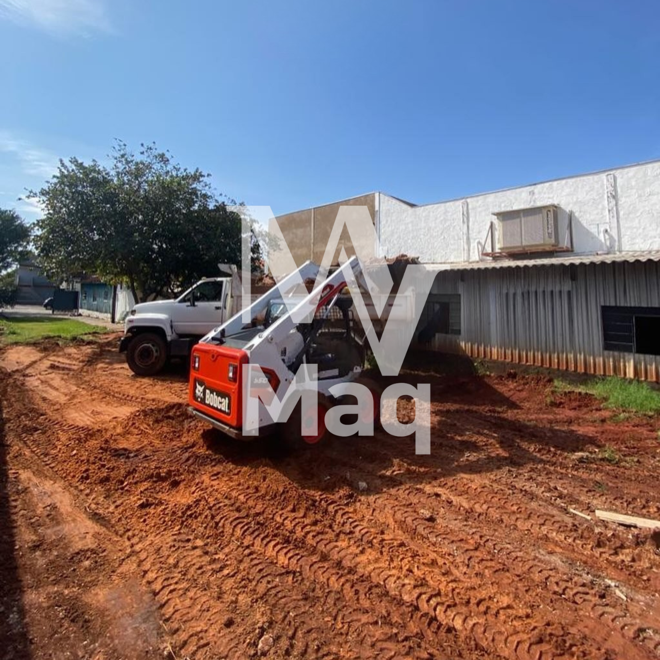 Bobcat preparando terreno ao lado de caminhão em obra