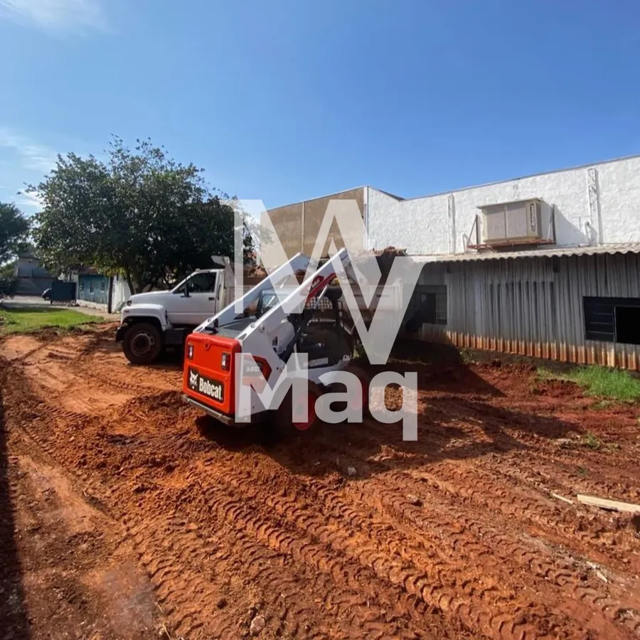 Bobcat preparando terreno ao lado de caminhão em obra