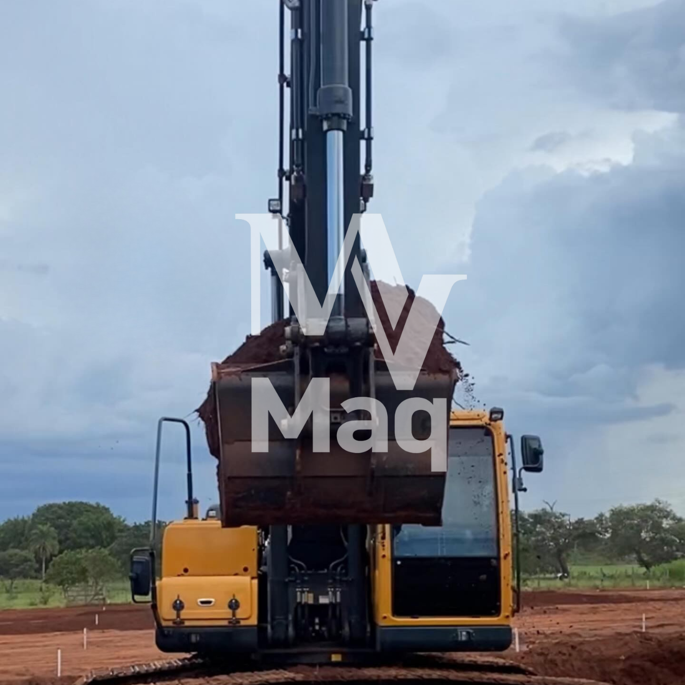 Escavadeira com caçamba carregada de terra em serviço de terraplenagem